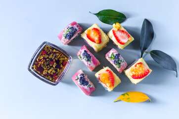 Bright rolls with seafood and fruit on a blue background top view. Colored buns, dark sauce and leaf decor on a colored background
