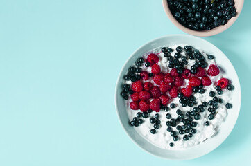 Healthy breakfast cottage cheese with sour cream and berries in a light dish on a light background.
