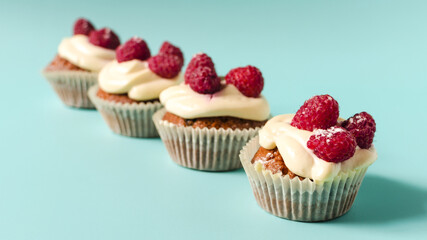 Cupcakes with white cream and raspberries lined up on a blue background sharpness in the foreground. Sweet homemade cupcakes on a colored background close-up.