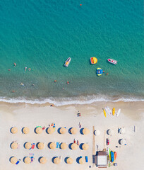 Sand beach aerial view directly above, vertical shot. Sunbeds, sunshades and water sports equipment, people swimming and taking sunbath