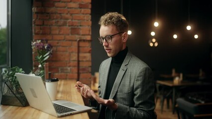 Caucasian young attractive businessman sitting in cafe near office center working on laptop and have a video call. Man talking on video conference online indoors. High quality 4k footage