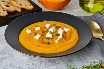 Traditional autumn pumpkin creamy puree soup with feta cheese, seeds, thyme, toast and olive oil. Delicious cucurbita mashed meal. Thanksgiving tasty fall dish. Horizontal, side view, closeup