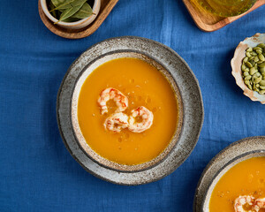 Seasonal pumpkin creamy puree soup with prawns. Pascetarian delicious autumn meal. Tradiitonal thanksgiving mashed gourd dish. Tasty cucurbita in ceramic bowl on linen background