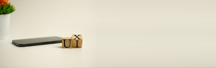 Wooden cube on a white table with letters UX, UI. Concept of development and design and development, user interface, user experience, software, app. Copy space on right for design, Blurred background.