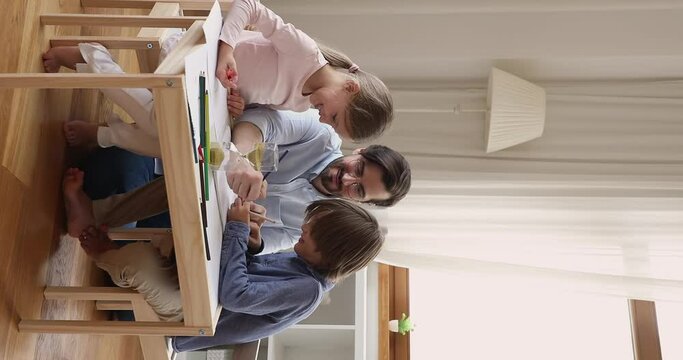 Single father enjoy spending leisure time with children preteen daughter son having fun painting colorful pictures. Male tutor teach little pupils to draw using pencils in playful way. Vertical video