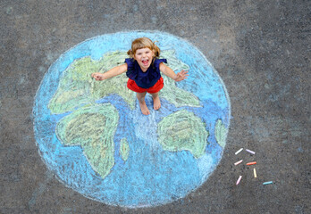 Little preschool girl with earth globe painting with colorful chalks on ground. Positive toddler child. Happy earth day concept. Creation of children for saving world, environment and ecology.