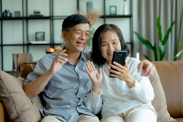 Happy elderly Asian couple doing facetime video calling with a smartphone at home using the zoom...