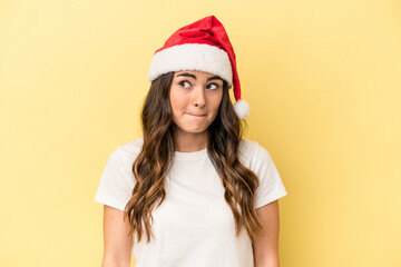 Young caucasian woman celebrating Christmas isolated on yellow background confused, feels doubtful and unsure.
