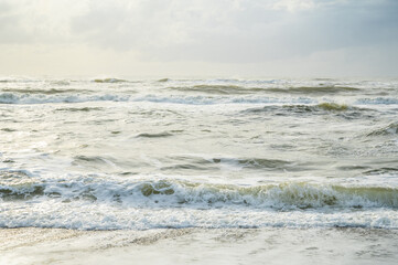 Troubled sea, breaking waves and green water flooded with golden light in the sunset.