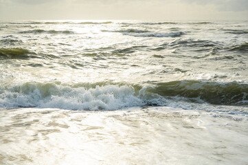 Troubled sea, breaking waves and green water flooded with golden light in the sunset.