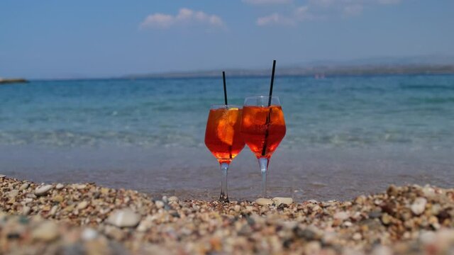 glass of aperol spritz cocktail stands on sand near the sea