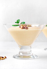 Mango dessert with yogurt topped with pistachio and mint in glass bowl on the white table
