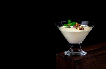 Mango dessert with yogurt topped with pistachio and mint in glass bowl against the black background. Copy space