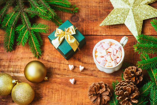 Christmas background. Spruce branches, Christmas balls, cup with coffee with marshmallows, golden star and gift on a wooden background. Copy space Top view. Christmas or New Year's card. flat lay