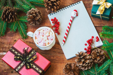 Christmas background. Spruce branches, red berries, notebook, gifts, and cup with marshmallows on a wooden background. Copy space Top view. Christmas or New Year's card. flat lay