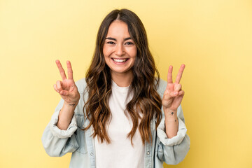 Young caucasian woman isolated on yellow background showing victory sign and smiling broadly.