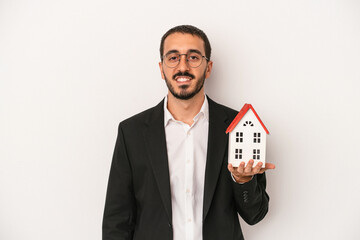 Young real estate agent man holding a model house isolated on white background happy, smiling and...