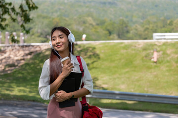 Happy young beautiful asian woman wearing headset and holding notebook in park.