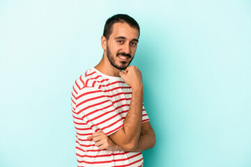 Young caucasian man isolated on blue background smiling happy and confident, touching chin with hand.