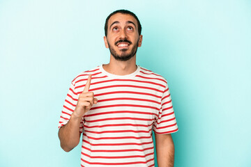 Young caucasian man isolated on blue background indicates with both fore fingers up showing a blank...