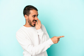 Young caucasian man isolated on blue background saying a gossip, pointing to side reporting something.