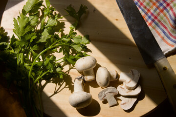 Kitchen board with rolled and whole mushrooms next to some parsley sprigs and a knife