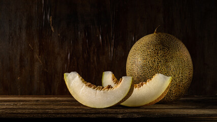 ripe round gulabi melon with slices on a wooden table on a dark old brown background. dark artistic still life in simple rustic style with copy space