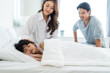 Asian loving parents take care of sleeping daughter in bedroom at home. 