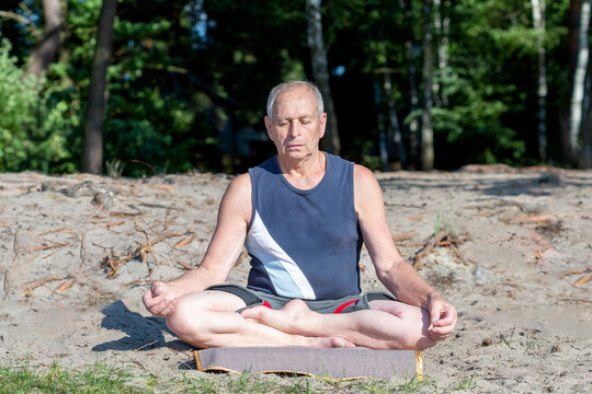 An elderly man practices yoga on the beach. Healthy Lifestyle.