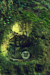 Medallion of Jesus Christ in a carved mossy rock face in a forest.