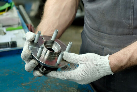 Spare parts for a passenger car.In the hands of an auto mechanic, a new hub assembly with a bearing.Inspection of the suspension part before replacement during repair and maintenance of the car.