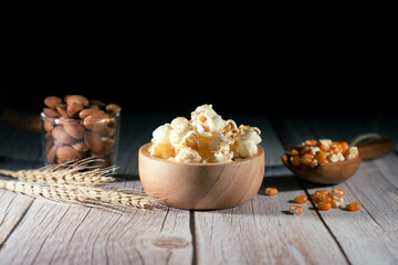 Sweet caramel popcorn in a wooden bowl with almonds and dry corn on a dark background