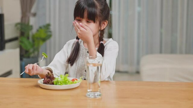 Unhappy Asian young girl don't want to eat vegetables on dinner plate. 