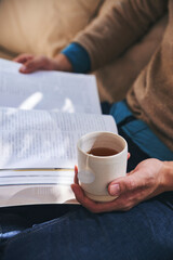 Fototapeta na wymiar Enjoying tea time reading a book while holding tea cup