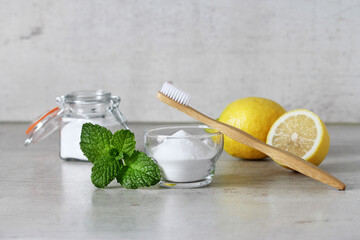 Teeth whitening ingredients at home. Baking soda, lemon and bamboo toothbrush on a gray concrete background. 