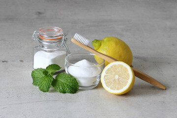 Baking soda, lemon, mint leaves and bamboo toothbrush on a gray concrete background  for teeth whitening at home.  - obrazy, fototapety, plakaty