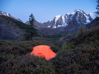 Gowing orange tent at dusk in the mountains. Cozy camping in the cool autumn mountains.
