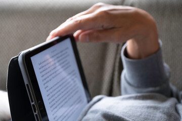 Person is lying on the sofa and holding the tablet with one hand while reading