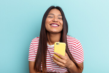 Young Venezuelan woman holding mobile phone isolated on blue background laughing and having fun.