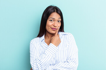 Young Venezuelan woman isolated on blue background looking sideways with doubtful and skeptical expression.