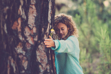 Young woman hugging tree with eyes closed in forest. Beautiful caucasian woman embracing tree with...