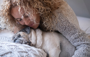 Young woman hugging her pet dog while sleeping on bed. Close up of woman and her dog pug sleeping on bed together. Woman and pet dog sleeping on cozy bed at home