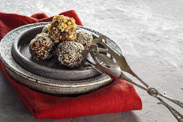 Oatmeal energy balls covered with sesame seeds and walnut crumbs in close-up, lie on a ceramic plate next to cooking tongs for serving. Copy space, healthy eating, trend..