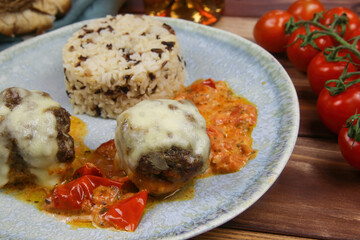 Closeup of blue plate on wood table with homemade minced meat balls gratinated with mozzarella cheese in fresh tomato sauce with rice