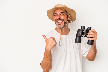 Middle age caucasian man holding binoculars isolated on white background  points with thumb finger away, laughing and carefree.