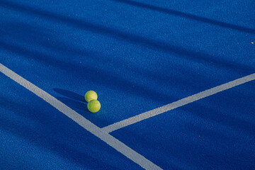 Two balls next to the lines of a paddle tennis court