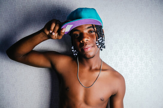 young dark-skinned man of Dominican Latino origin with braids in his hair, shirtless and wearing a cap