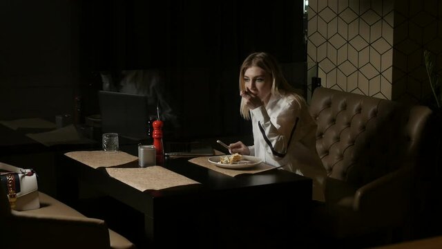 a lonely woman in a white shirt sits on a brown sofa in a restaurant cutting food and eating. High quality FullHD footage