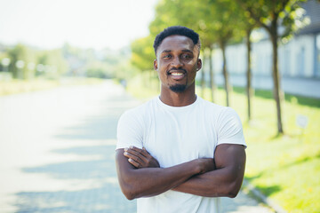 Fototapeta premium Young african american male athlete, on a morning jog, looks at the camera with his arms crossed, motivated and smiling