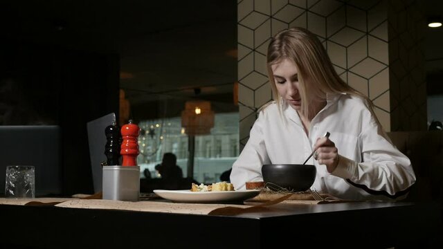 a young blonde woman eating soup sitting in a restaurant against a beige decorative wall. High quality FullHD footage